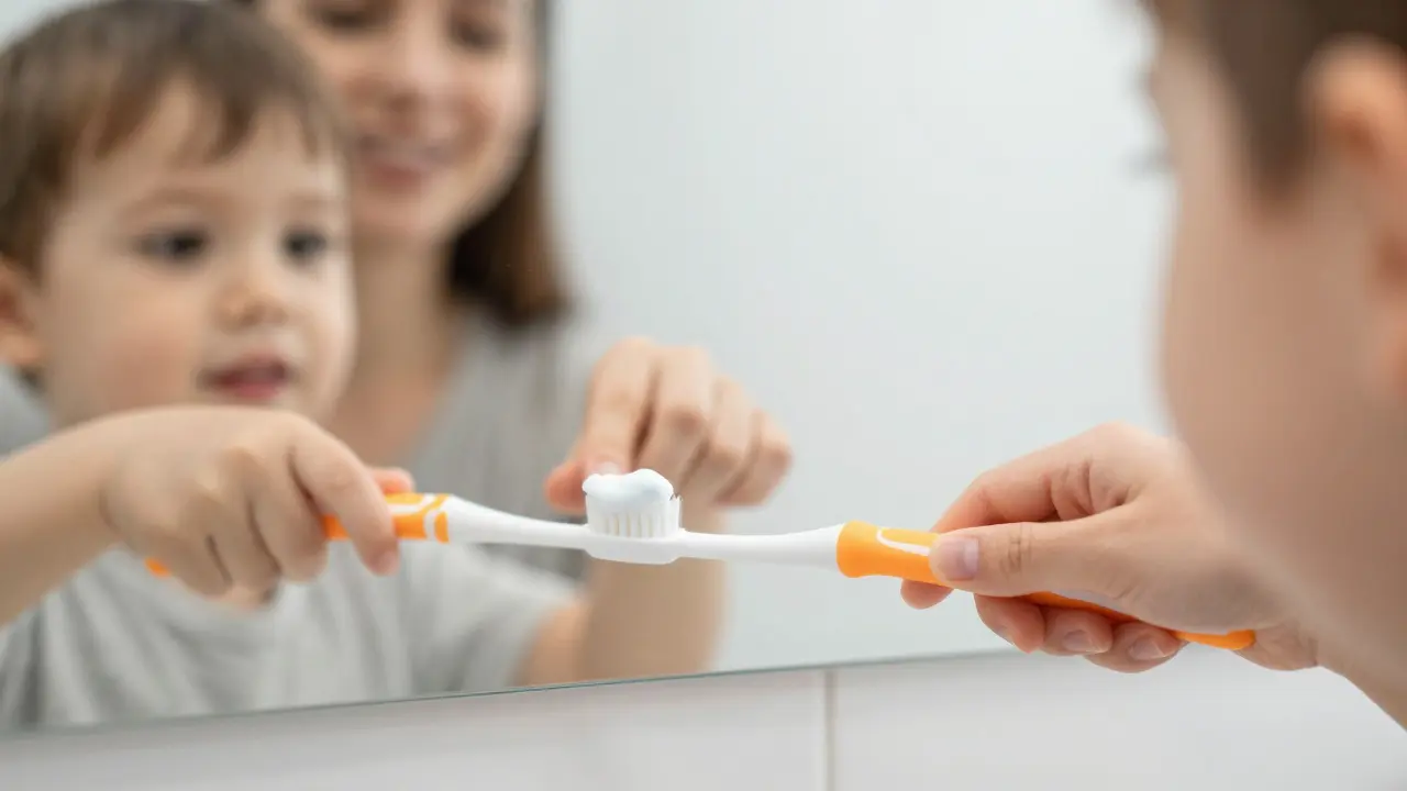 Malé dítě si čistí zuby pod dohledem rodiče v koupelně